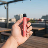 Hand holding an AirsPops ONE USE 6ml disposable vape outdoors during the day in a casual urban setting